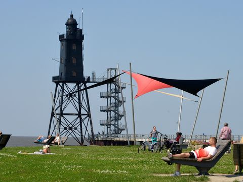 Ein ruhiger Moment auf der Leuchtturmwiese in Dorum-Neufeld, Spaziergänger genießen das Nordseeflair, während im Hintergrund der historische Leuchtturm Obereversand über dem Geschehen wacht. Natur, Weite und maritimer Charme vereinen sich zu einem typischen Bild der Küste.