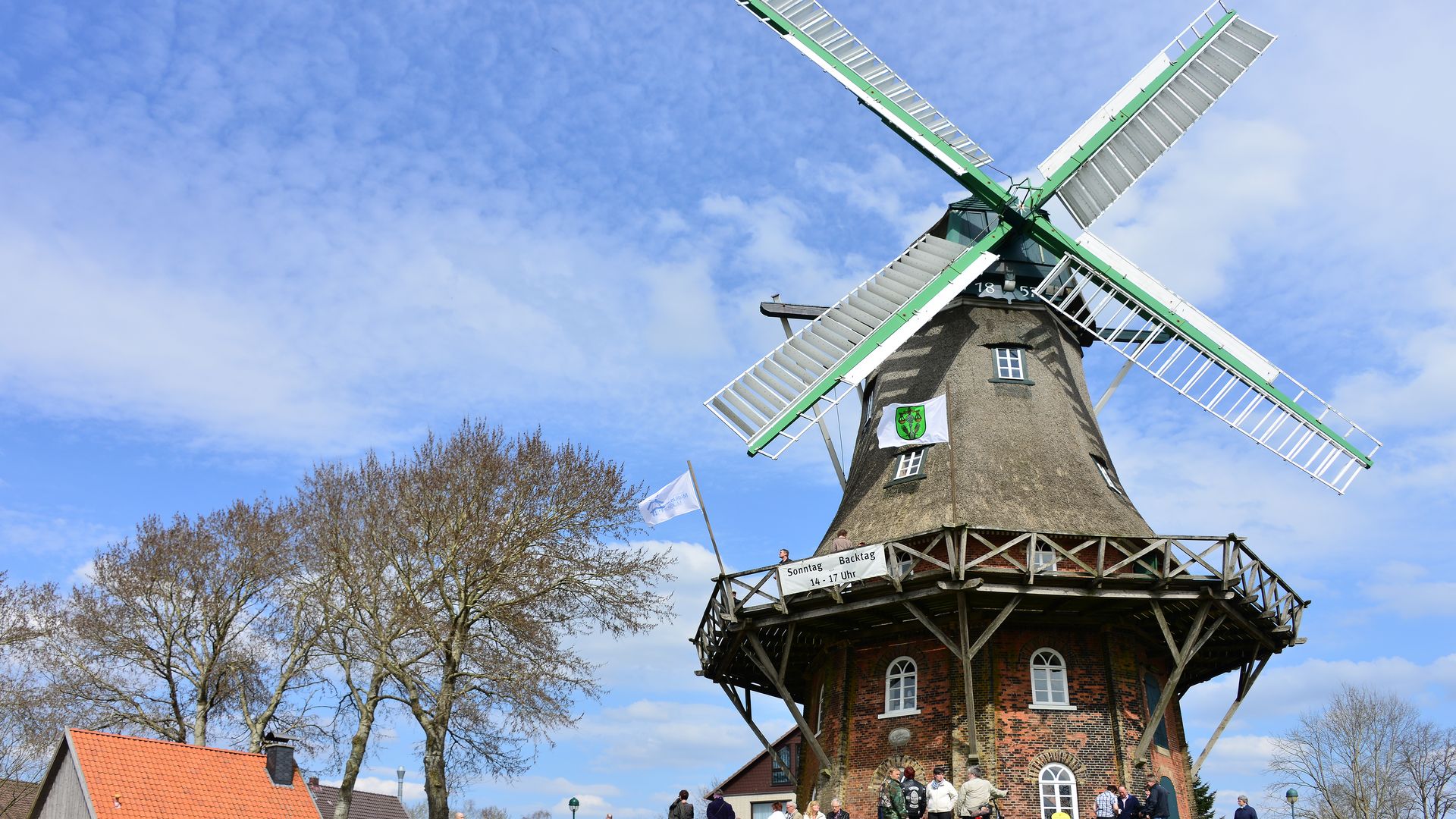 Die Galerie-Holländer Mühle in Midlum während einer Veranstaltung: Die historische Windmühle mit ihren großen Flügeln steht im Mittelpunkt der Szene. Rund um den Mühlenfuß haben sich zahlreiche Menschen versammelt.