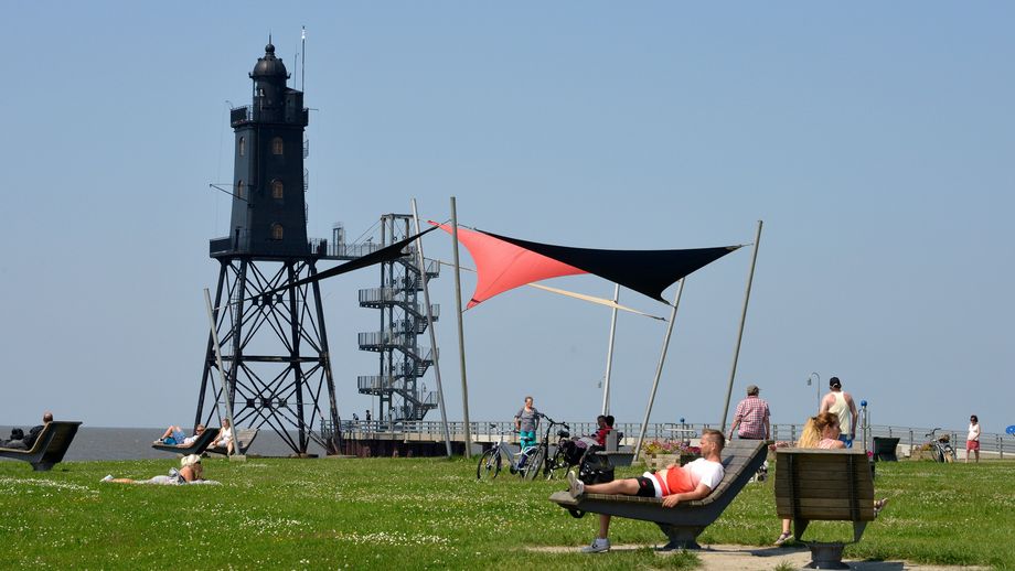 Ein ruhiger Moment auf der Leuchtturmwiese in Dorum-Neufeld, Spaziergänger genießen das Nordseeflair, während im Hintergrund der historische Leuchtturm Obereversand über dem Geschehen wacht. Natur, Weite und maritimer Charme vereinen sich zu einem typischen Bild der Küste.