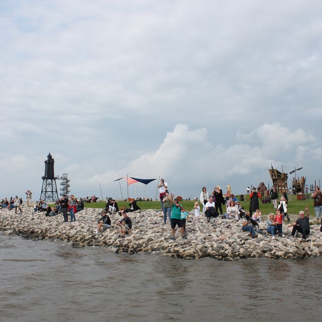Aus der Perspektive eines Kutters aufgenommen: Beim Auslaufen des Kutterkorsos 2023 säumen zahlreiche Besucher die Kaimauern, winken und bestaunen das Spektakel. Im Hintergrund ragt der Leuchtturm empor und verleiht der Szene maritimen Charme – ein stimmungsvoller Moment voller Tradition und Begeisterung