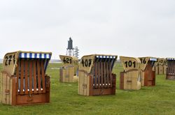 Am Grünstrand in Dorum-Neufeld sind mehrere geschlossene Strandkörbe zu sehen. Im Hintergrund erkennt man den Leuchtturm Obereversand.